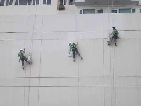 Three technicians painting a white exterior wall from their ropes