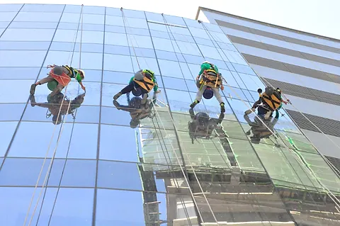 Four URABES technicians cleaning a glass curtain wall, reflected in the glass