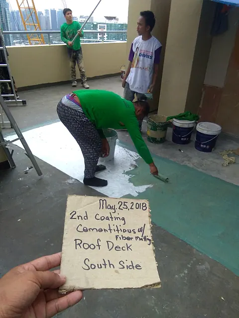 Second coat of cementitious waterproofing being brushed onto a roof deck