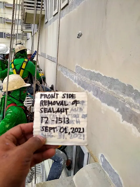 Failed sealant cut out of a wall joint, with the job label held up for the record
